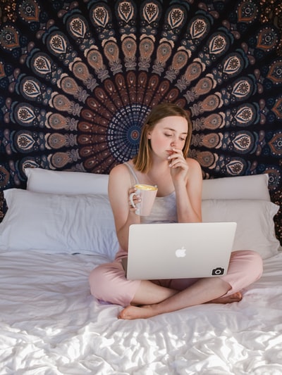 Sitting on the bed with a mug with MacBook woman
